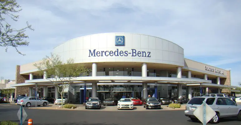 A mercedes benz dealership with cars parked in front of it.